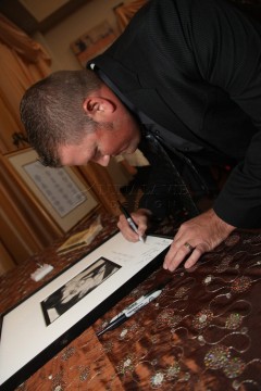 Man signing a large photograph on a table.