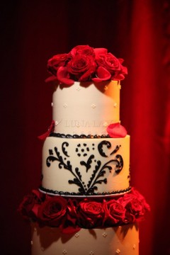 Elegant two-tier cake adorned with red roses and black intricate designs.