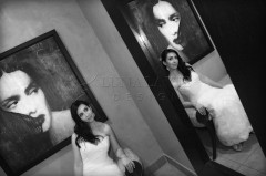 Black and white photo of a woman in a white dress looking at her reflection in a mirror.